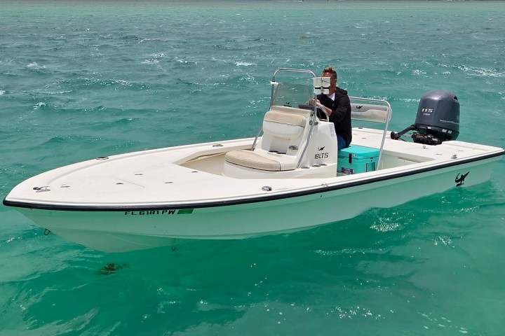 Person steering a white motorboat on clear turquoise water.