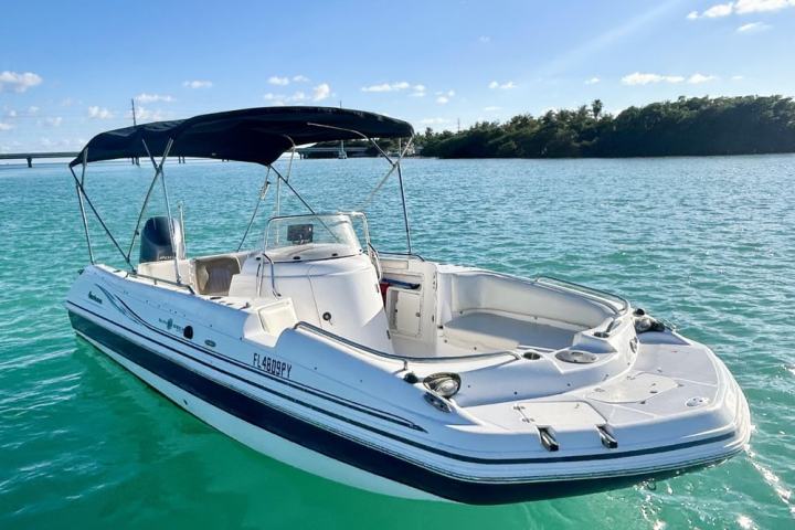 White speedboat with a canopy floating on clear turquoise water under a blue sky.